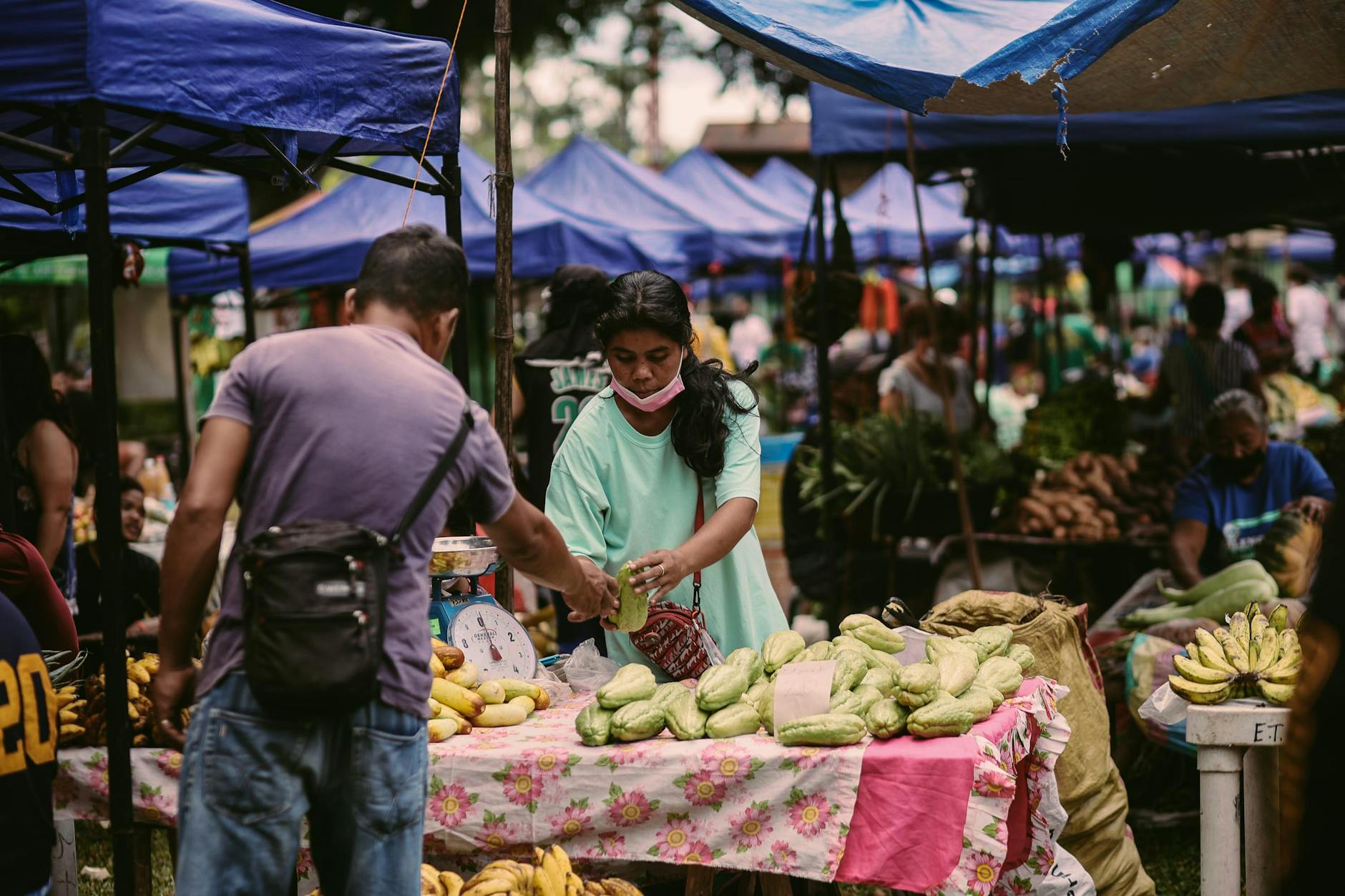 A busy outdoor farmers market with food stalls and shoppers