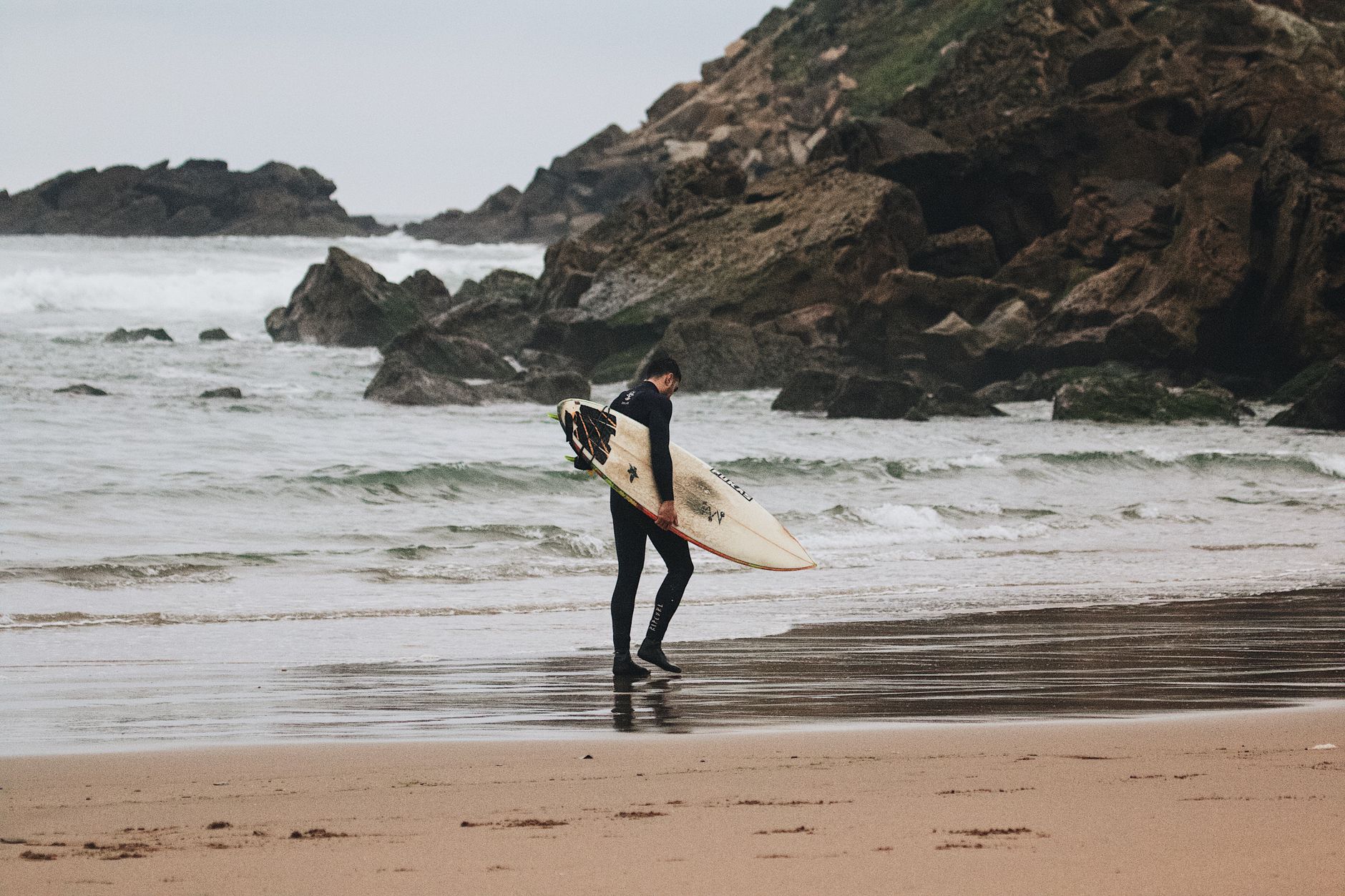 Surfer carrying a surfboard on a Cornwall beach